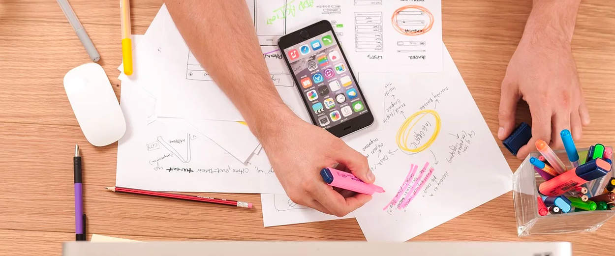 Person highlighting notes on desk with smartphone nearby.