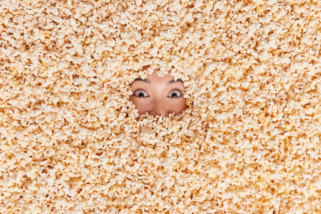 Person's face peeks through pile of popcorn.
