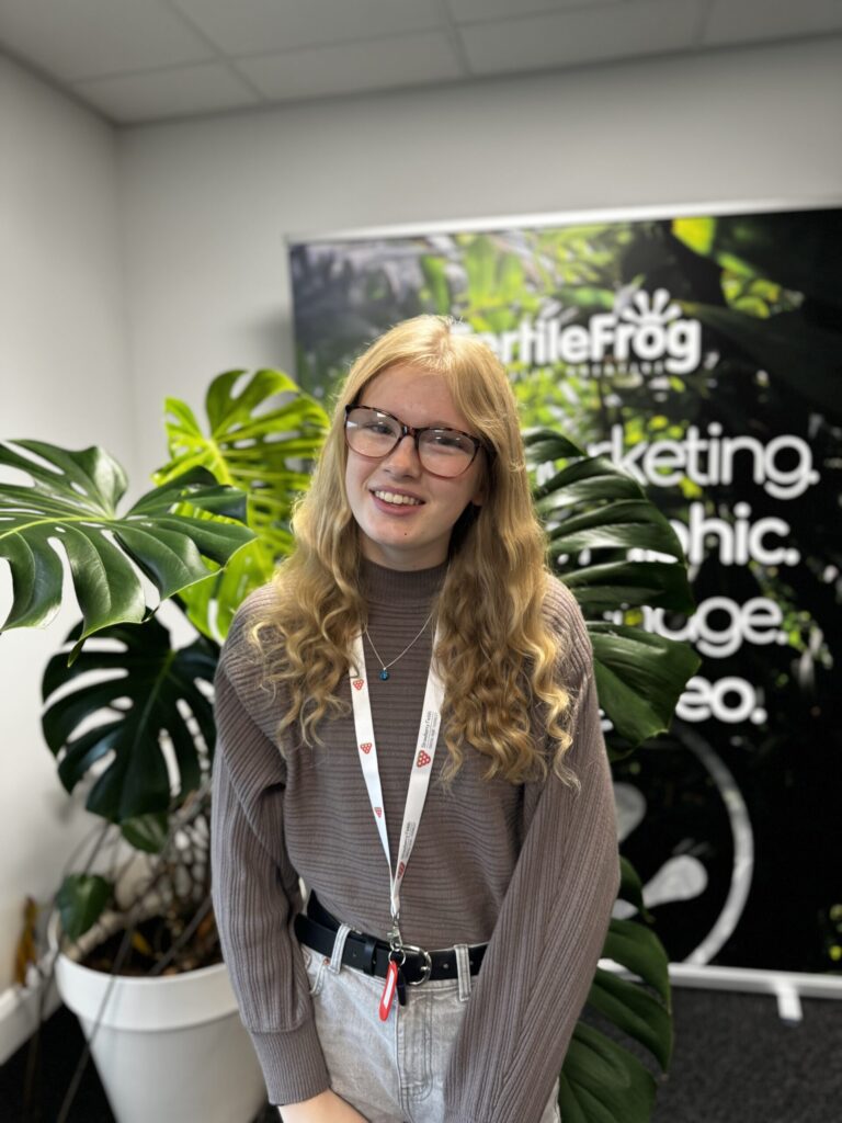 Person smiling in office with leafy plants.