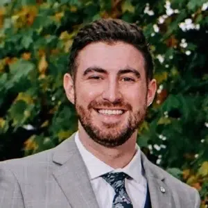 Man smiling in front of green leafy background.